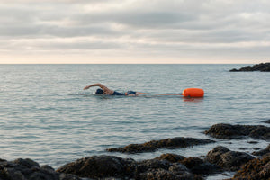 Swimmer towing the high-visibility orange safety float in open water